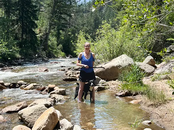 Dog standing calmly beside Kathleen in a natural stream setting in St. Vrain river, Colorado.